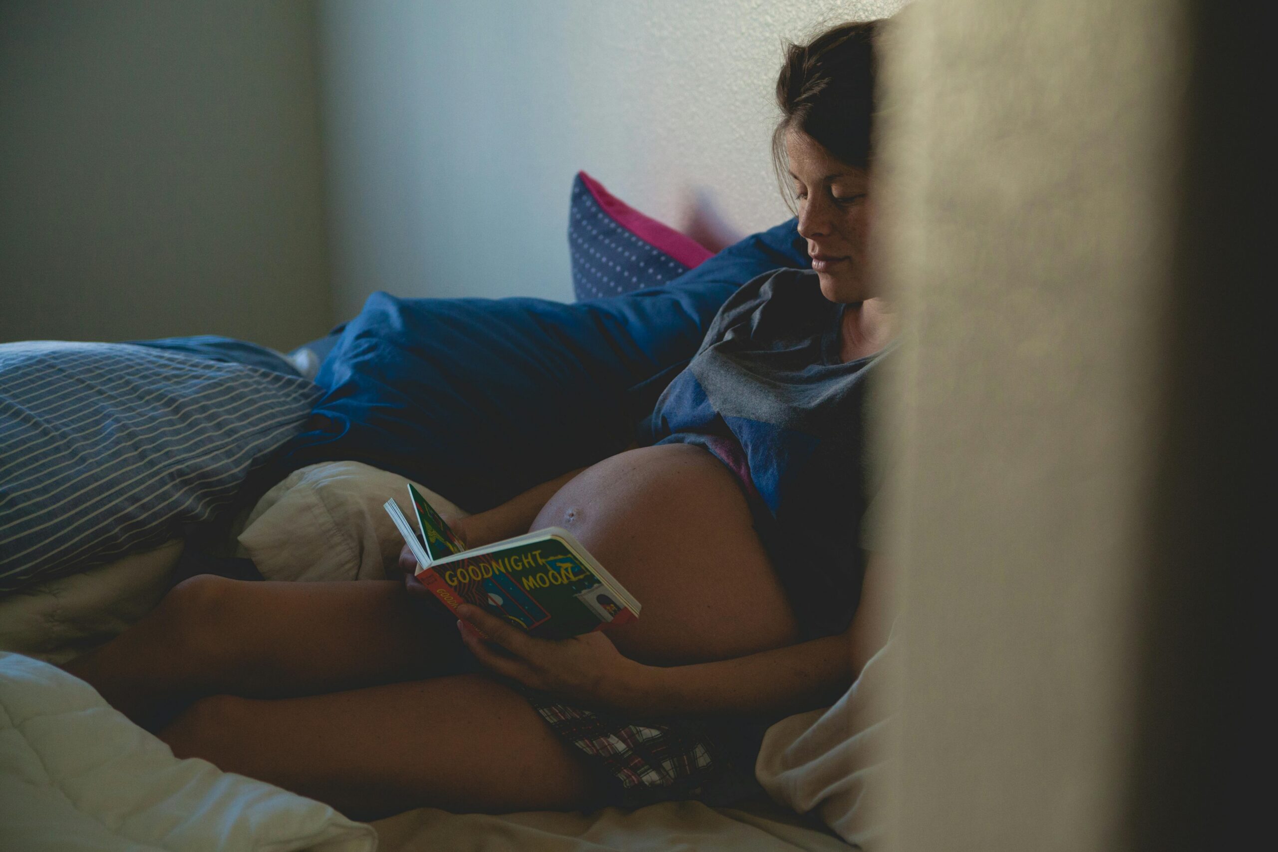 Pregnant woman reading on bed, enjoying a calm and intimate moment.